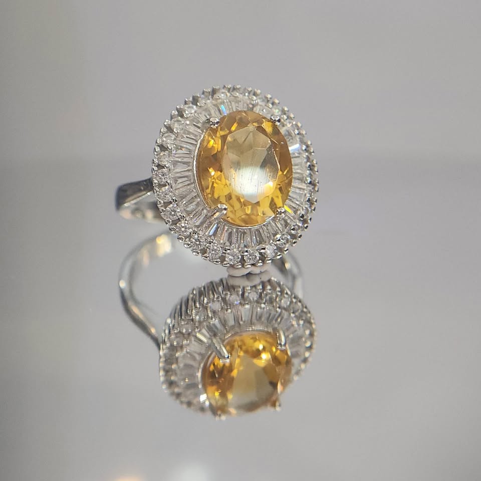 Silver ring with a yellow gemstone on a reflective surface