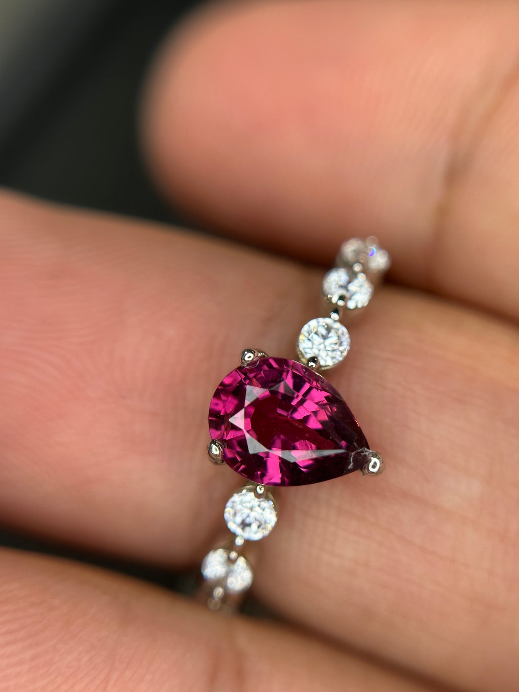 Ring with a pink teardrop-shaped gemstone and smaller white stones on a finger.