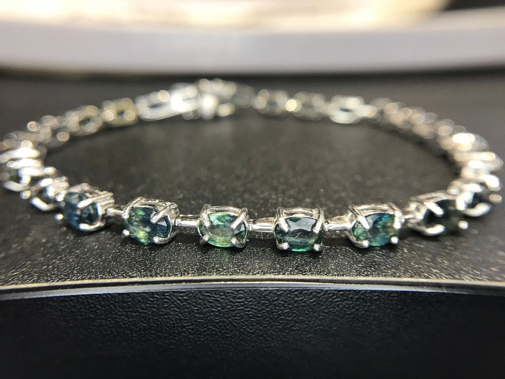 Shiza Gems oval teal sapphires and cubic zirconia tennis bracelet in sterling silver. Blue-green stones with sparkling accents.