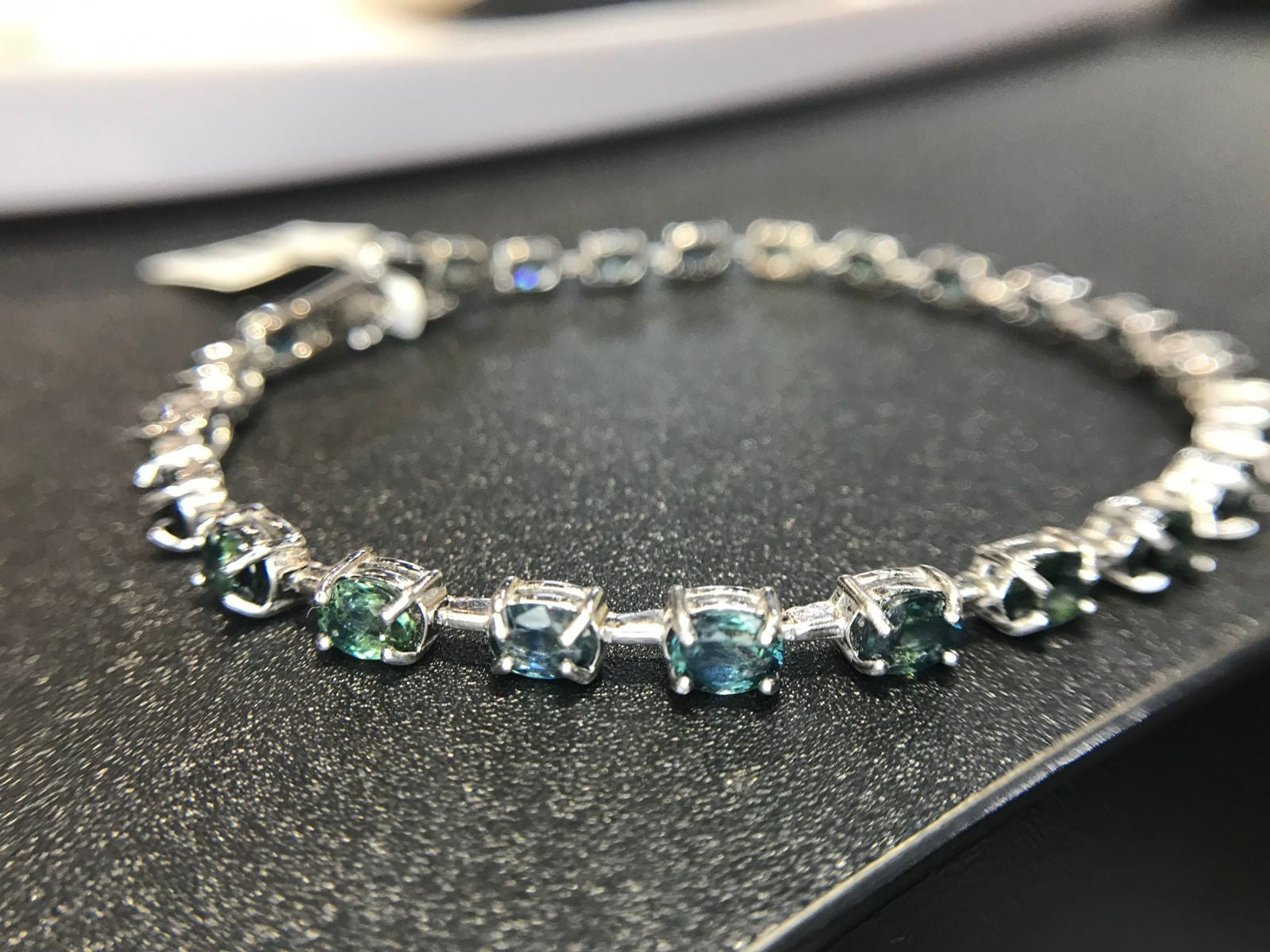 Shiza Gems oval teal sapphire and cubic zirconia tennis bracelet in sterling silver. Blue-green stones.