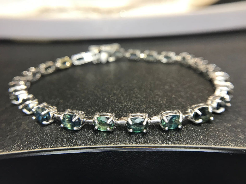 Shiza Gems oval teal sapphires and cubic zirconia tennis bracelet in sterling silver. Blue-green stones with sparkling accents.