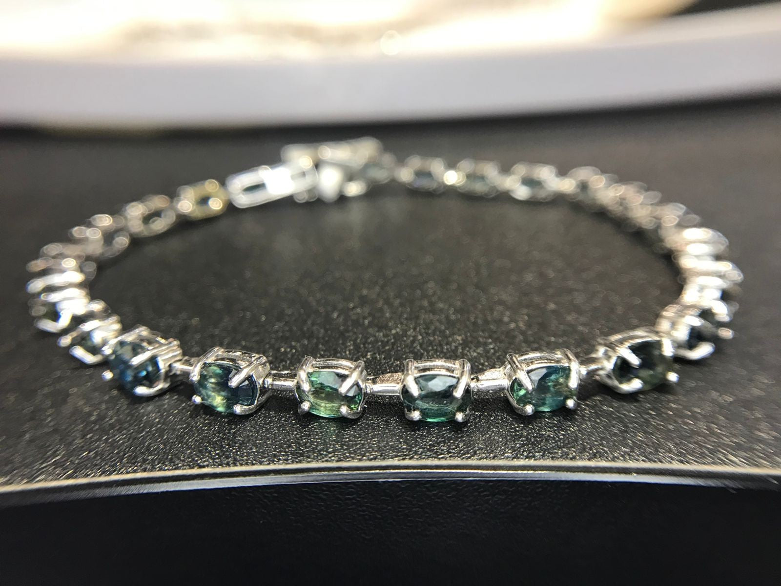 Shiza Gems oval teal sapphires and cubic zirconia tennis bracelet in sterling silver. Blue-green stones with sparkling accents.