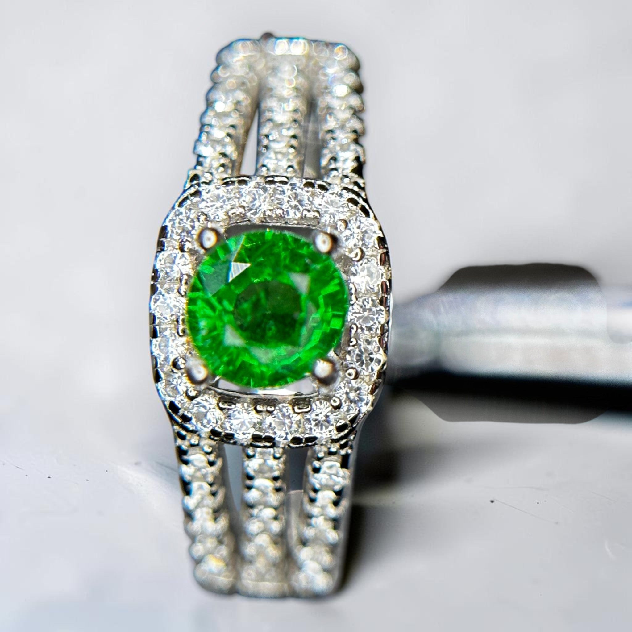 Shiza Gems Tsavorite silver ring with a central green gemstone surrounded by small diamonds. Features a split band design.