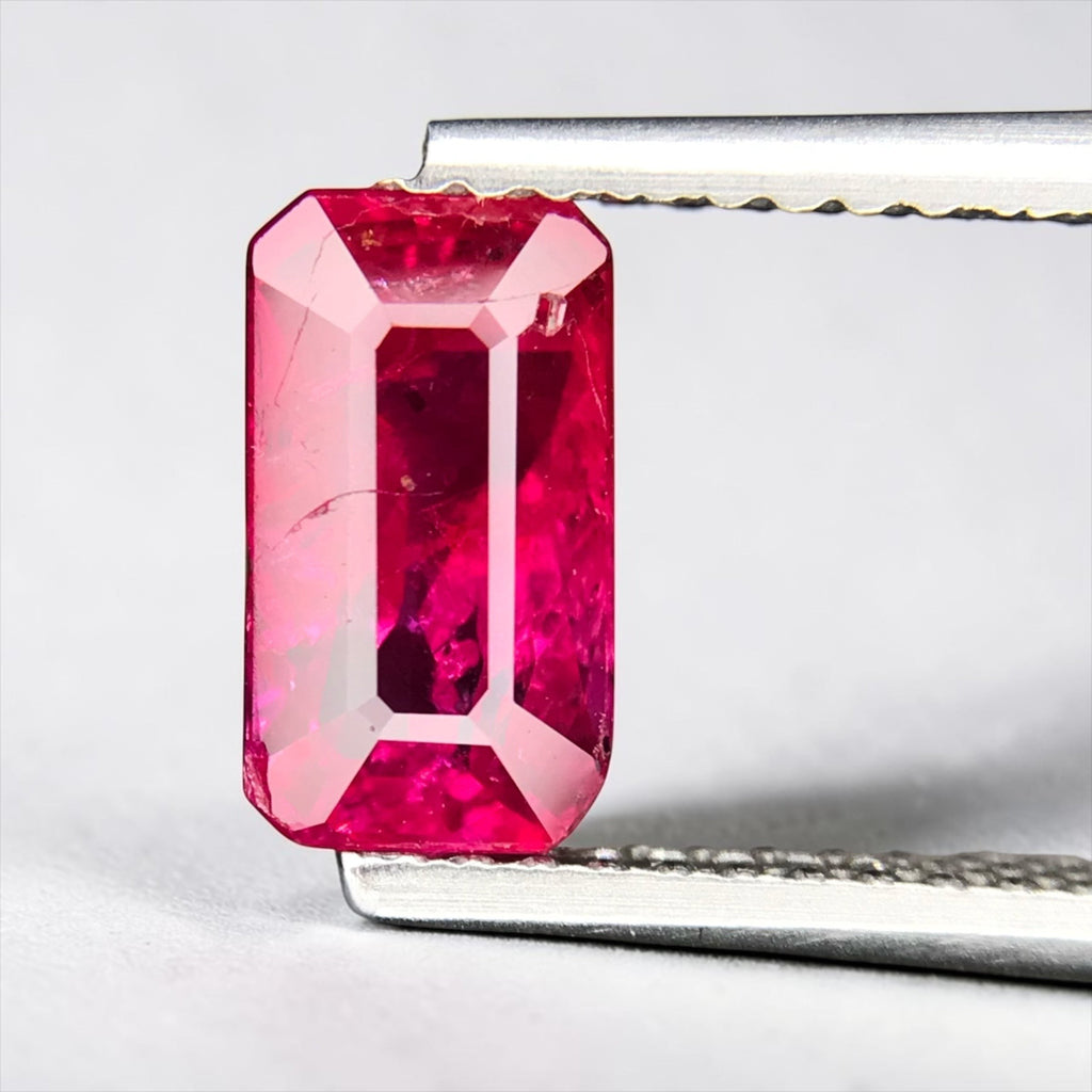 Shiza Gems 2.01 ct emerald-cut vivid pinkish-red unheated ruby gemstone held in tweezers.