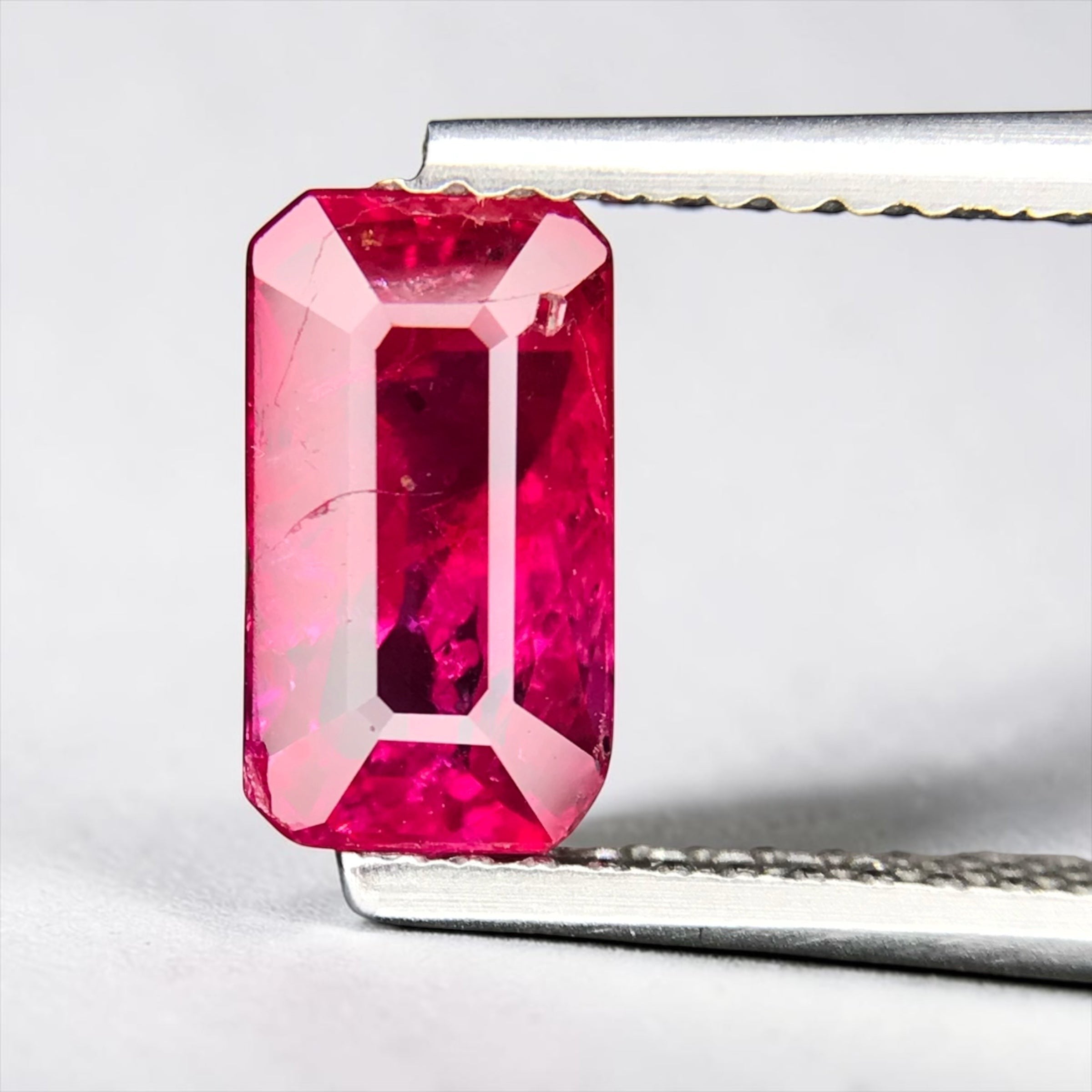 Shiza Gems 2.01 ct emerald-cut vivid pinkish-red unheated ruby gemstone held in tweezers.